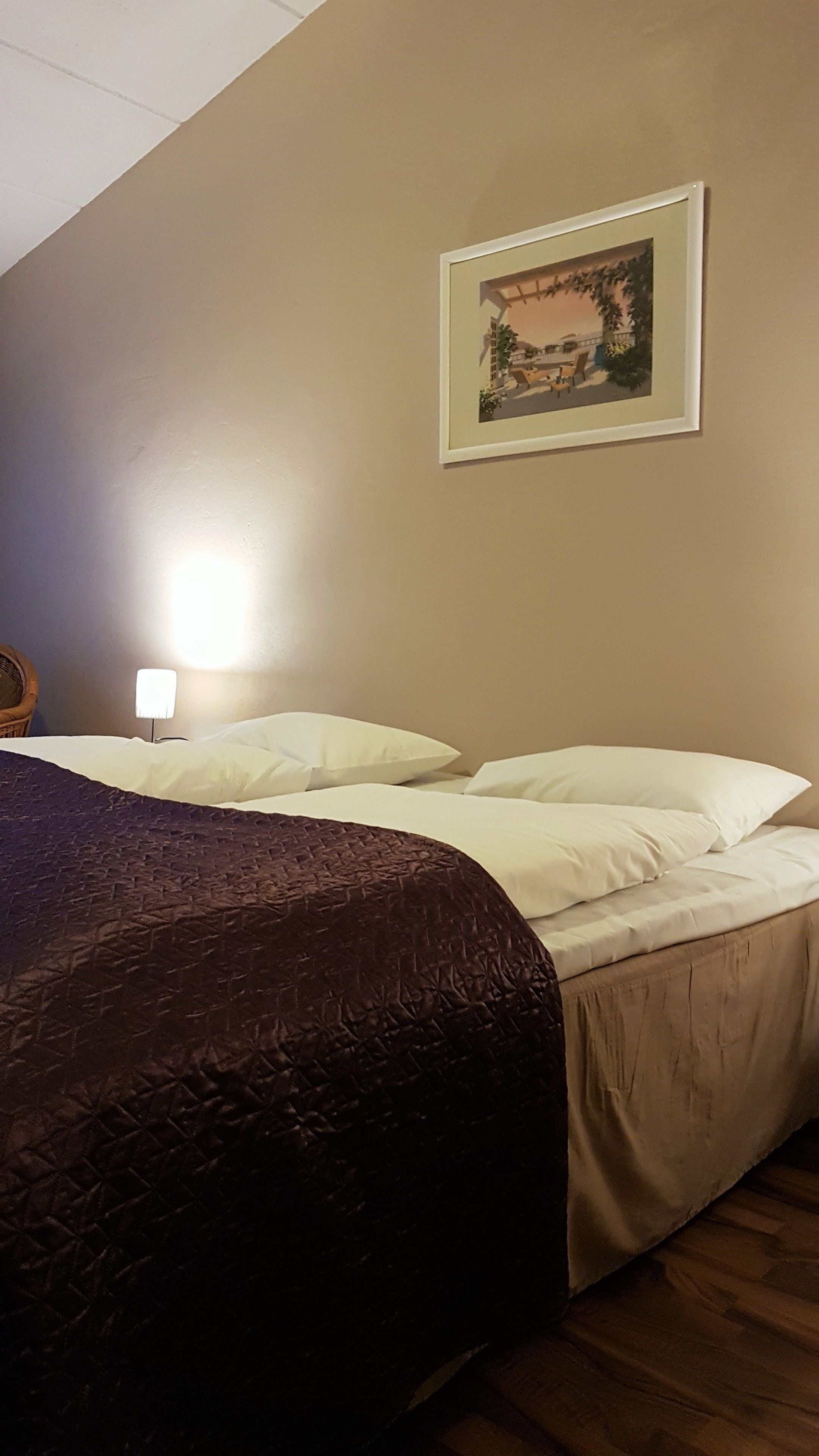 A hotel room with a bed, a nightstand with a lamp, and a framed picture on the wall.