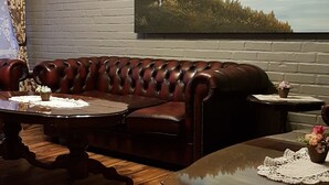 A living room with a leather sofa, a glass coffee table, and a painting of a lake on the wall. - Bardu Hotell (Bardu)