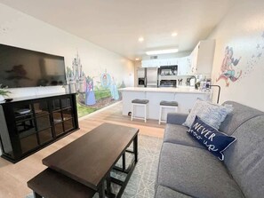 Una sala de estar con sofá, mesa de centro y televisor. Cuenta con una cocina equipada con refrigerador y microondas.