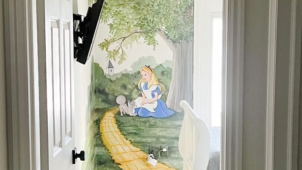 Un pasillo con un mural de escena de cuento de hadas, una silla blanca y un televisor de pantalla plana montado en la pared.