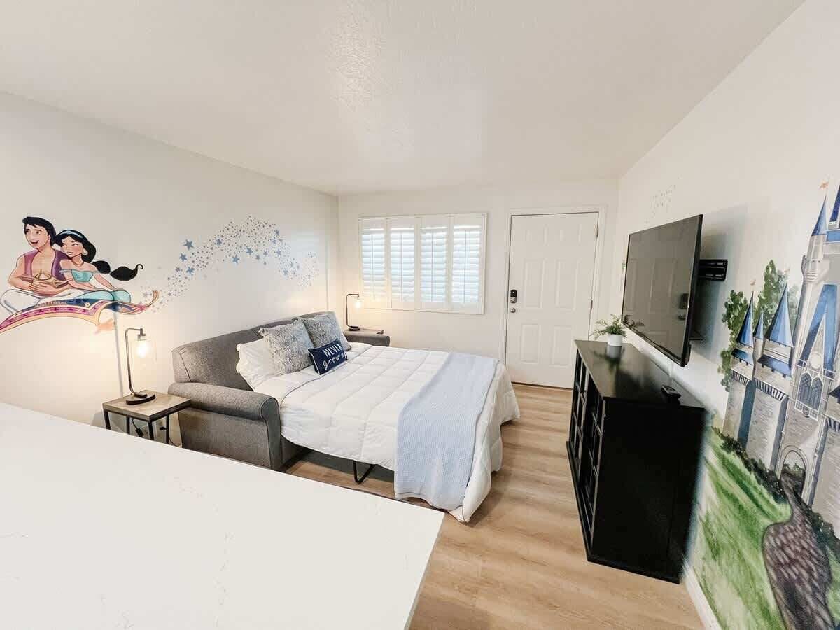 Quarto com cama, mesa de cabeceira, abajur e televisão.