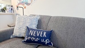 Un sofá gris con un cojín azul que dice 'NEVER grow up' y un adhesivo mural con una pareja y estrellas.