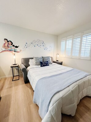 Une chambre à coucher comprenant un lit, des tables de chevet, un élément de décoration murale et une fenêtre avec des stores.