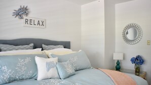 Une chambre à coucher comprenant un lit, des oreillers, un miroir fixé au mur, une table de chevet avec une lampe et un élément décoratif mural.