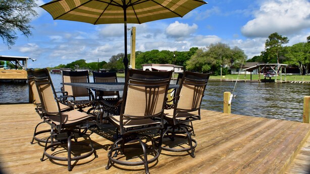 Une terrasse en bois avec une table et des chaises, un parasol et une vue sur un lac et des arbres.