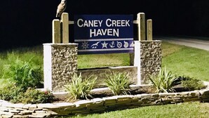 Une enseigne pour Caney Creek Haven, avec un oiseau perché au sommet, entourée de piliers en pierre et de verdure.
