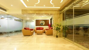 A modern lobby with a glass wall, a reception desk, and a seating area with sofas. - Hotel SRR Grand (Chengalpattu)