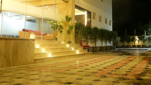 A modern building with geometric light patterns on the ceiling, a glass entrance, and a tiled courtyard with potted plants. - Hotel SRR Grand (Chengalpattu)