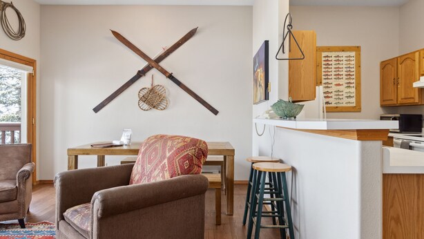 Una sala de estar acogedora con un sillón marrón, una mesa de comedor de madera y una zona de cocina con armarios de madera y un adorno de pared con motivos de peces.