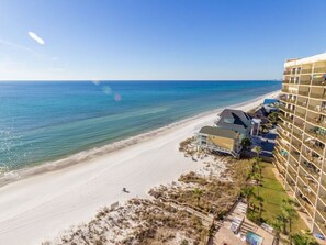Un hotel frente a la playa con varios balcones, una playa de arena y una vista despejada del océano.