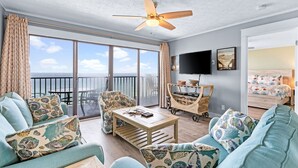 Een ruime woonkamer met een balkon, een plafondventilator, een flatscreen-tv en een bed met bloemenbeddengoed.