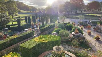 Ein Garten mit ordentlich geschnittenen Hecken, einem kreisförmigen Wasserspiel und einem gepflasterten Weg.
