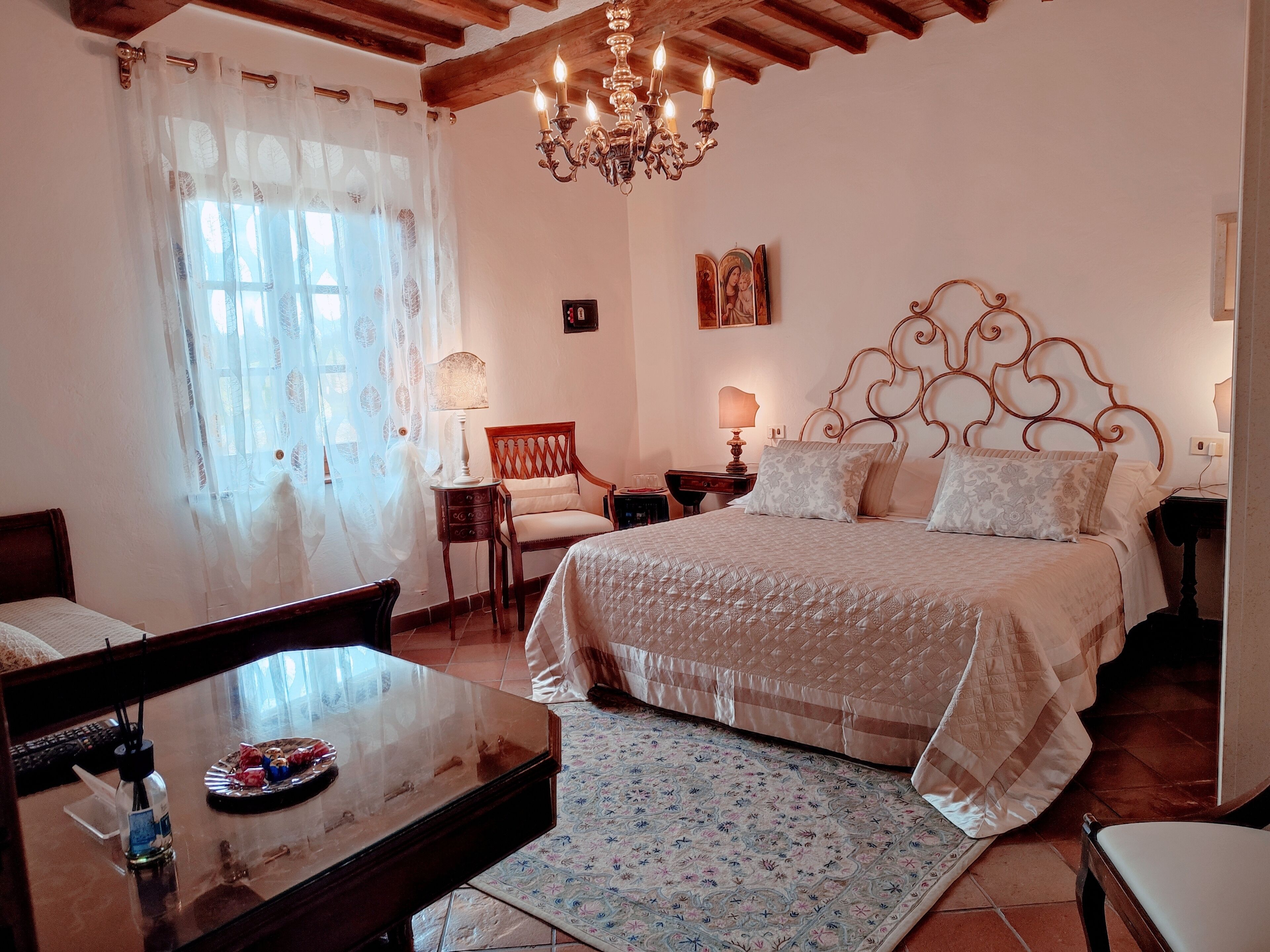 Camera da letto con un letto grande, una testiera in legno, un lampadario, una sedia, un tavolino con una bottiglia e un tappeto decorato.
