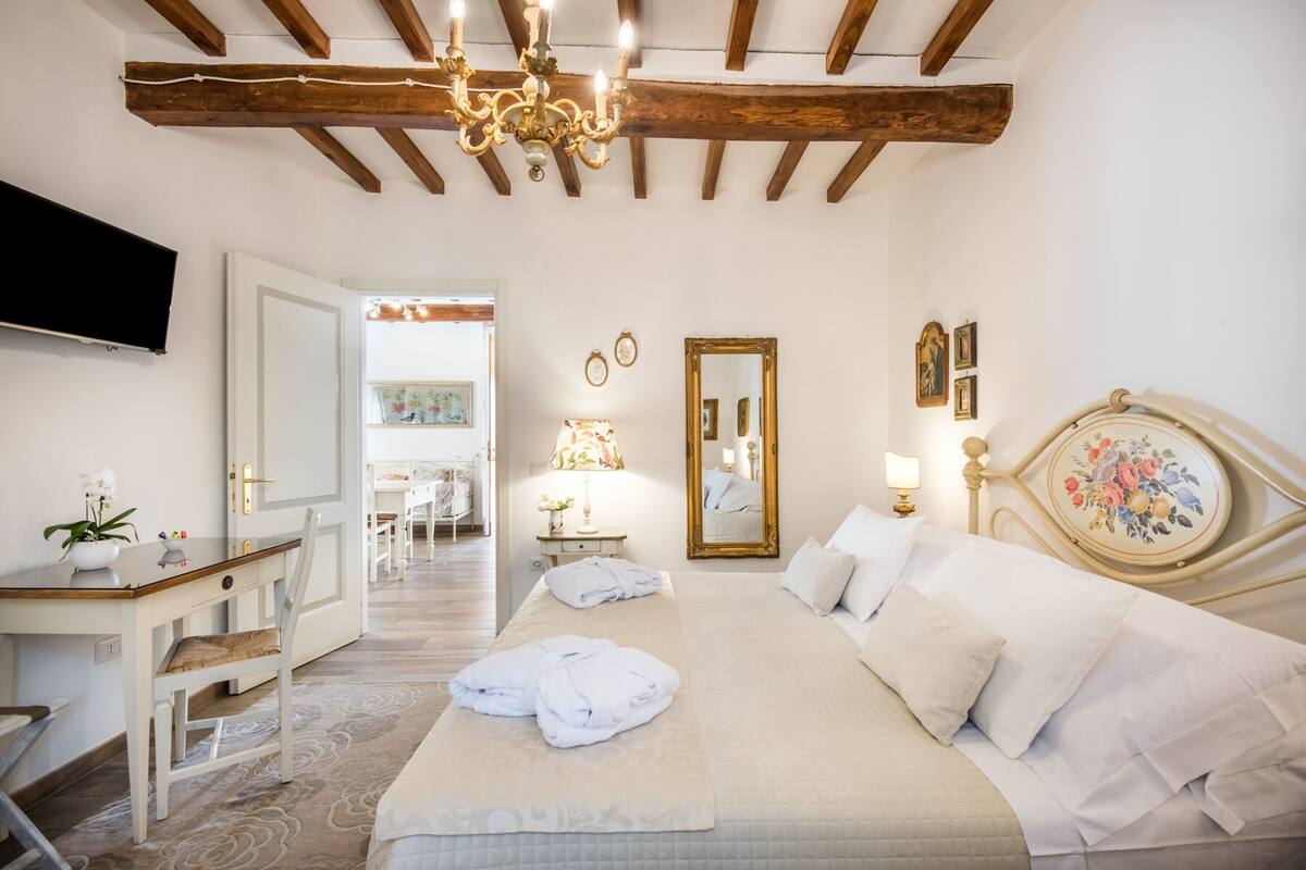 Un dormitorio con cama, mesita de noche, lámpara y espejo.