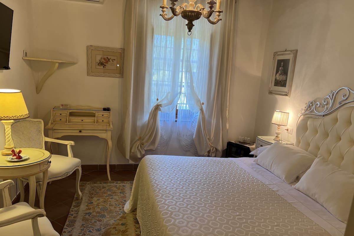 Una habitación de hotel con cama, escritorio, silla, mesita de noche y candelabro.