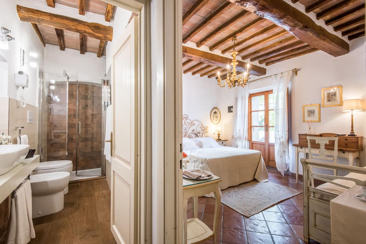 Un dormitorio con cama, mesita de noche, lámpara y una ventana con cortinas.