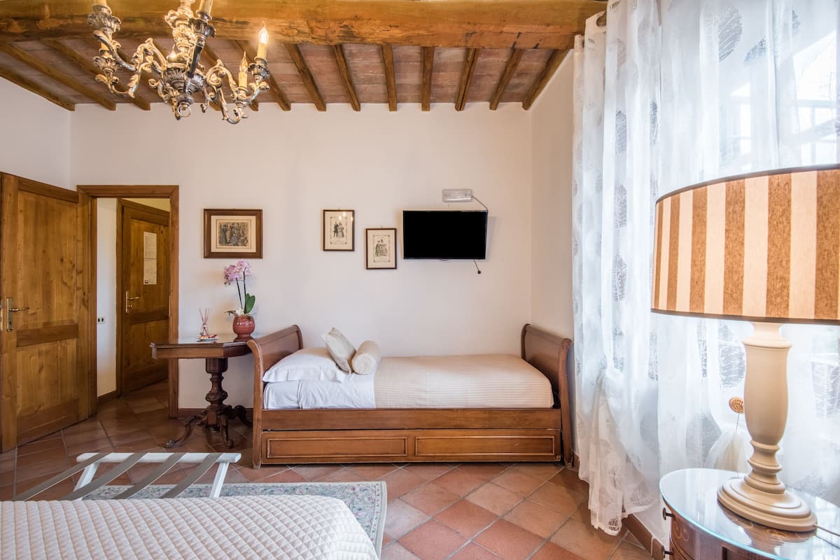 Un dormitorio con cama de madera, una mesita de noche, un televisor montado en la pared y una araña.