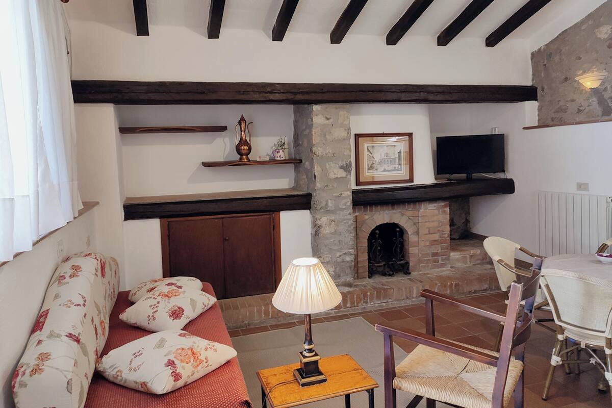 Una sala de estar con un sofá, una mesa con una lámpara, una chimenea y un televisor montado en la pared.