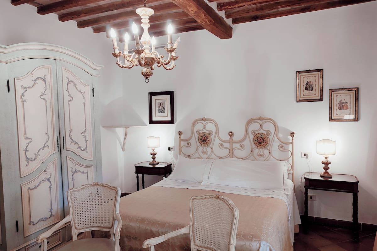 Un dormitorio con cama, dos mesitas de noche, un candelabro, un armario y dos sillas.
