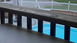 En vy över en trädgård med en pool, ett vitt staket och en byggnad i bakgrunden.