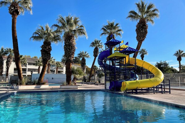 A swimming pool with a water slide and palm trees.