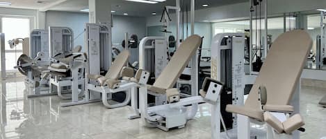 A gym with various exercise machines, a mirrored wall, and a tiled floor.