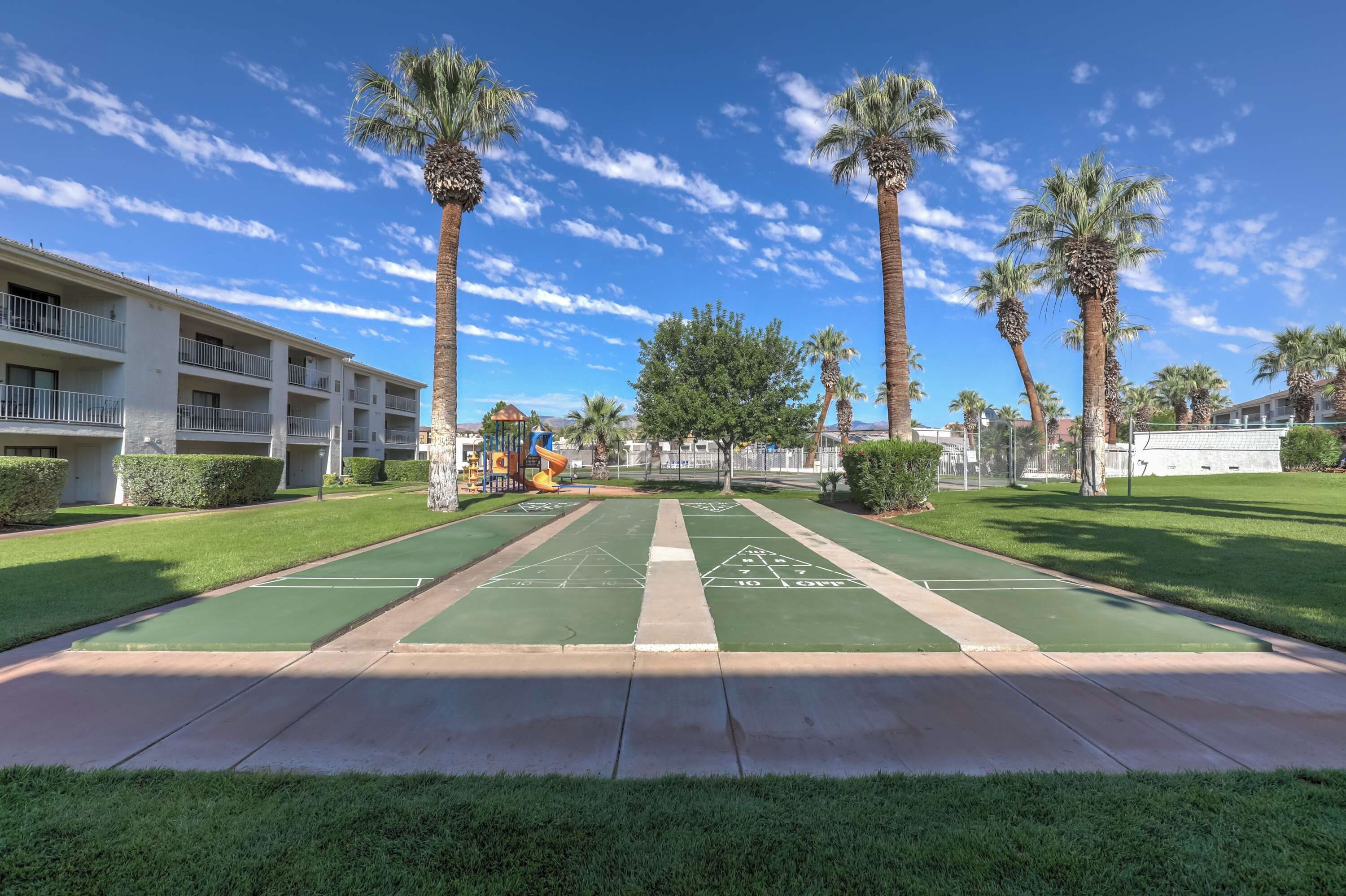 A courtyard with a shuffleboard court, palm trees, and a building with balconies.
