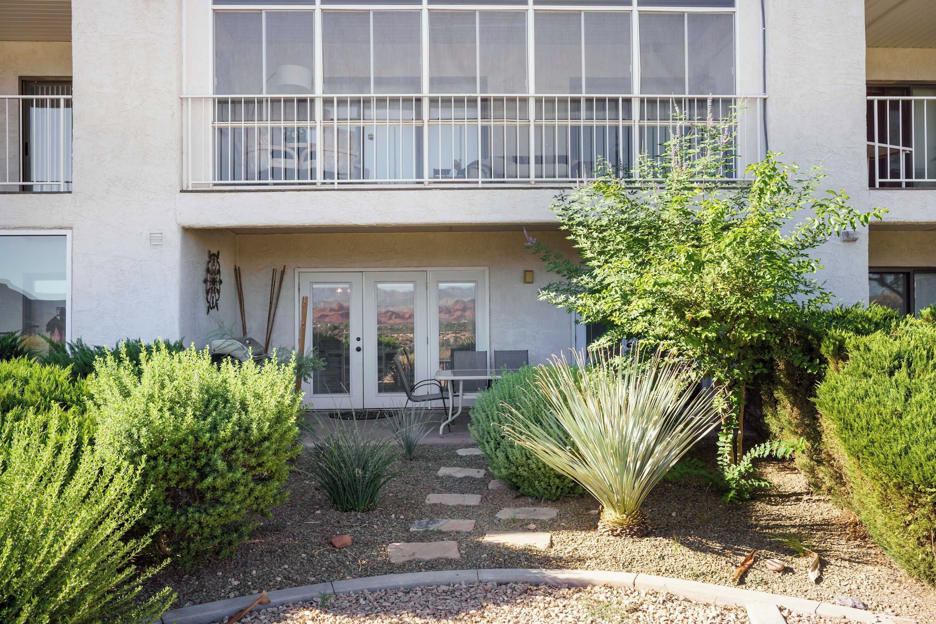 A two-story building with a balcony, a covered entrance, and a garden with various plants.