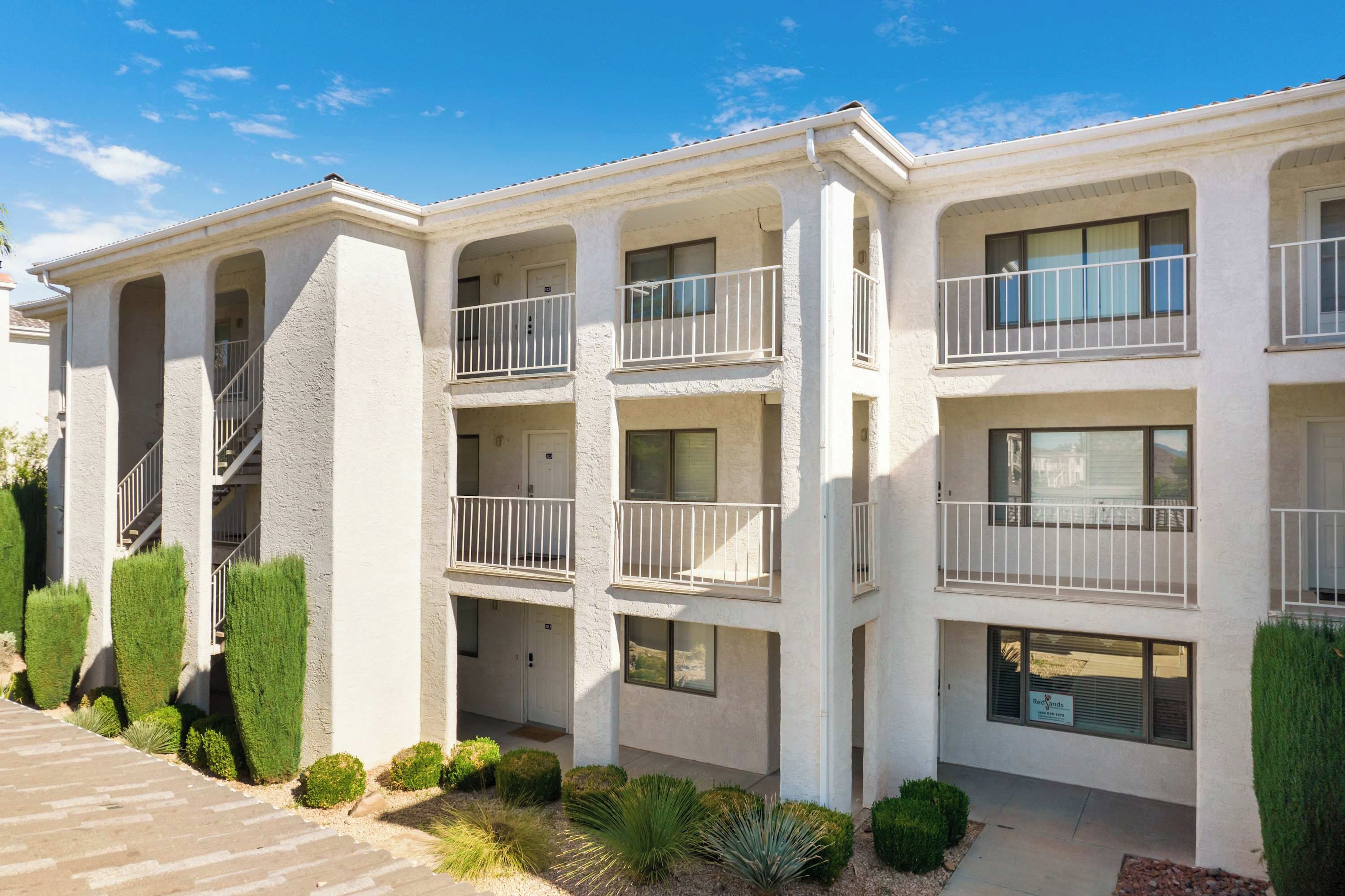 A multi-story residential building with balconies, a central staircase, and a landscaped front yard.