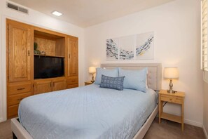 A bedroom with a bed, wooden wardrobe, artwork on the wall, and bedside lamps.