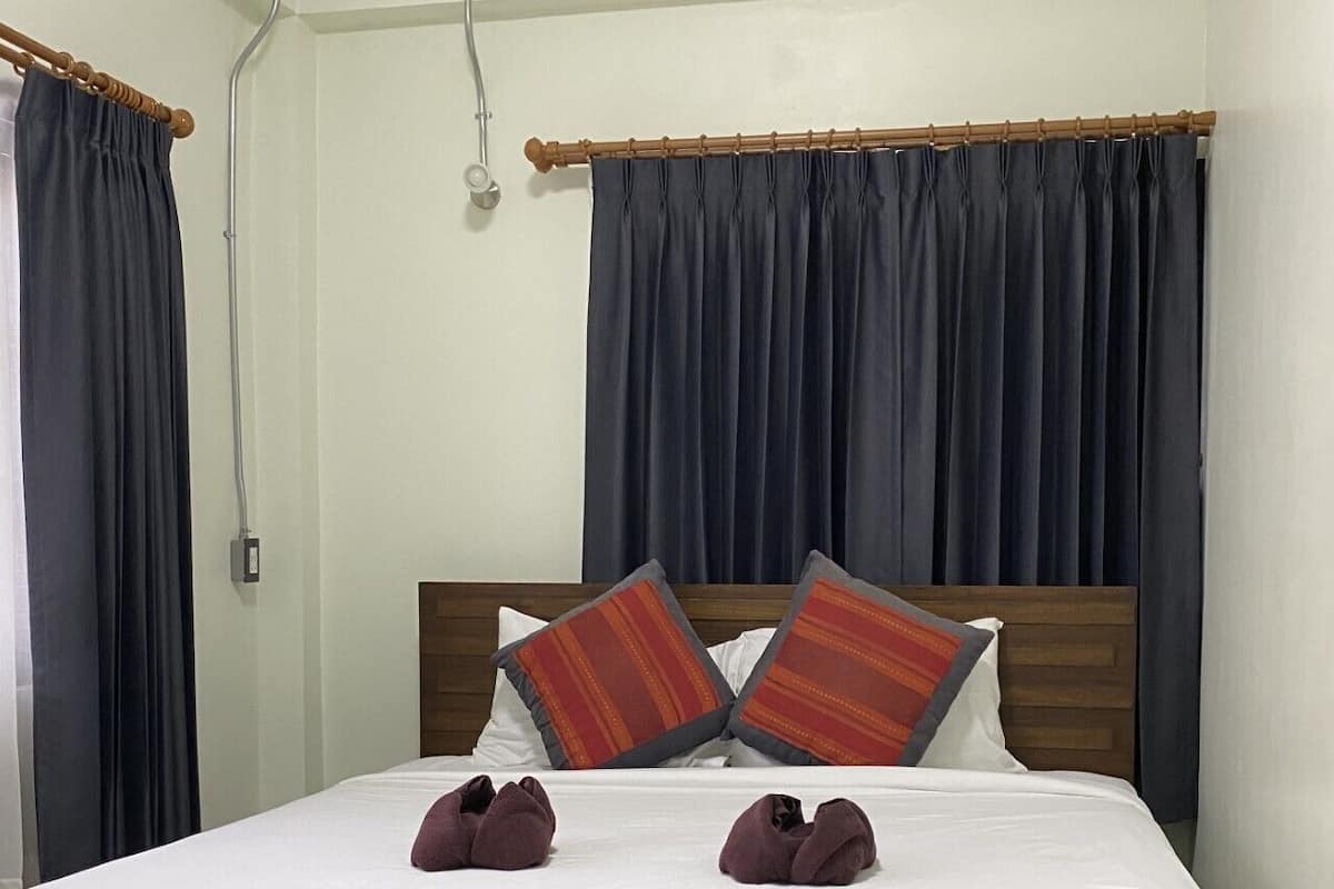A neatly made bed with white sheets and two pillows, a wooden headboard, and dark curtains.