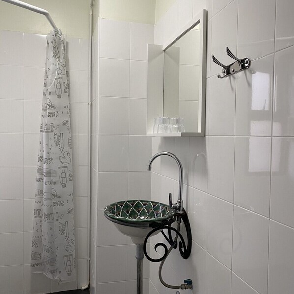 A bathroom with a shower curtain, a sink with a green mosaic bowl, a mirror, and a towel rack.