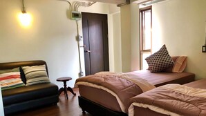 A room with two beds, a small table, a sofa, and a wall-mounted light fixture. - HP House Cafe' (Chiang Mai)