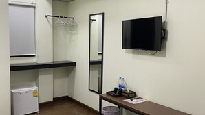 A small hotel room with a bed, a desk with a mirror, a television, a mini-fridge, and a trash bin. - HP House Cafe' (Chiang Mai)