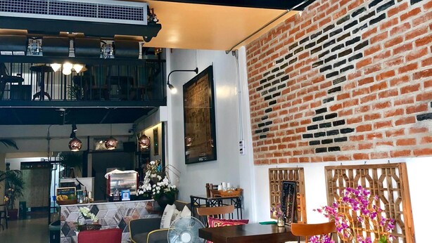 A spacious interior with a high ceiling, a chandelier, a brick wall, and a dining area with chairs and a table. - HP House Cafe' (Chiang Mai)