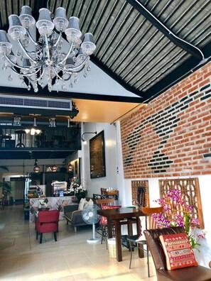 A spacious interior with a high ceiling, a chandelier, a brick wall, and a dining area with chairs and a table.