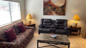 Un salon comprenant un canapé, deux fauteuils, une table basse et un tableau accroché au mur.
