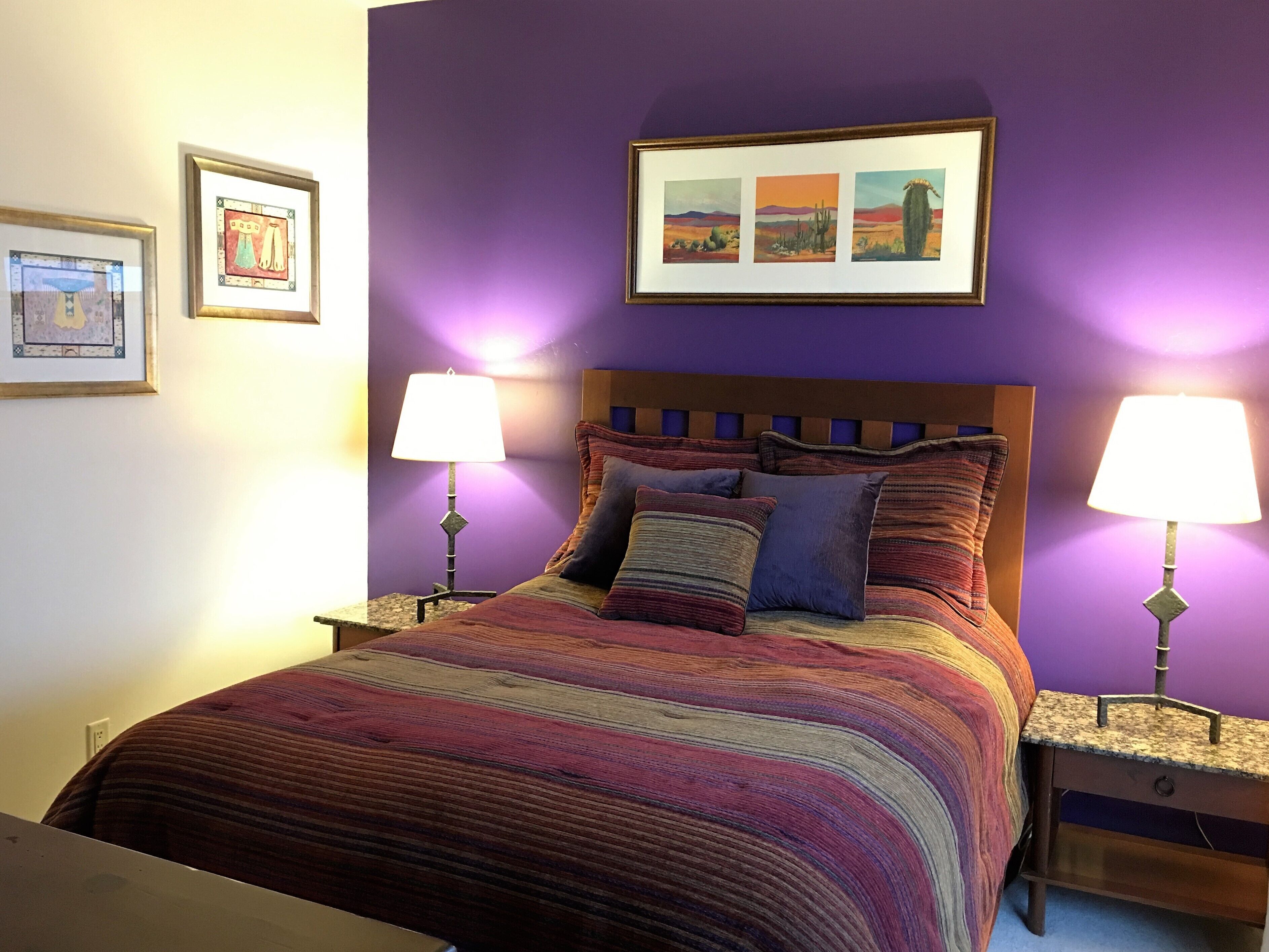 A bed with a colorful striped bedspread, two bedside lamps, and a framed picture above the bed.
