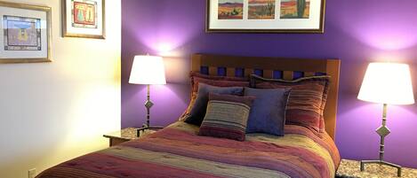 A bed with a colorful striped bedspread, two bedside lamps, and a framed picture above the bed.
