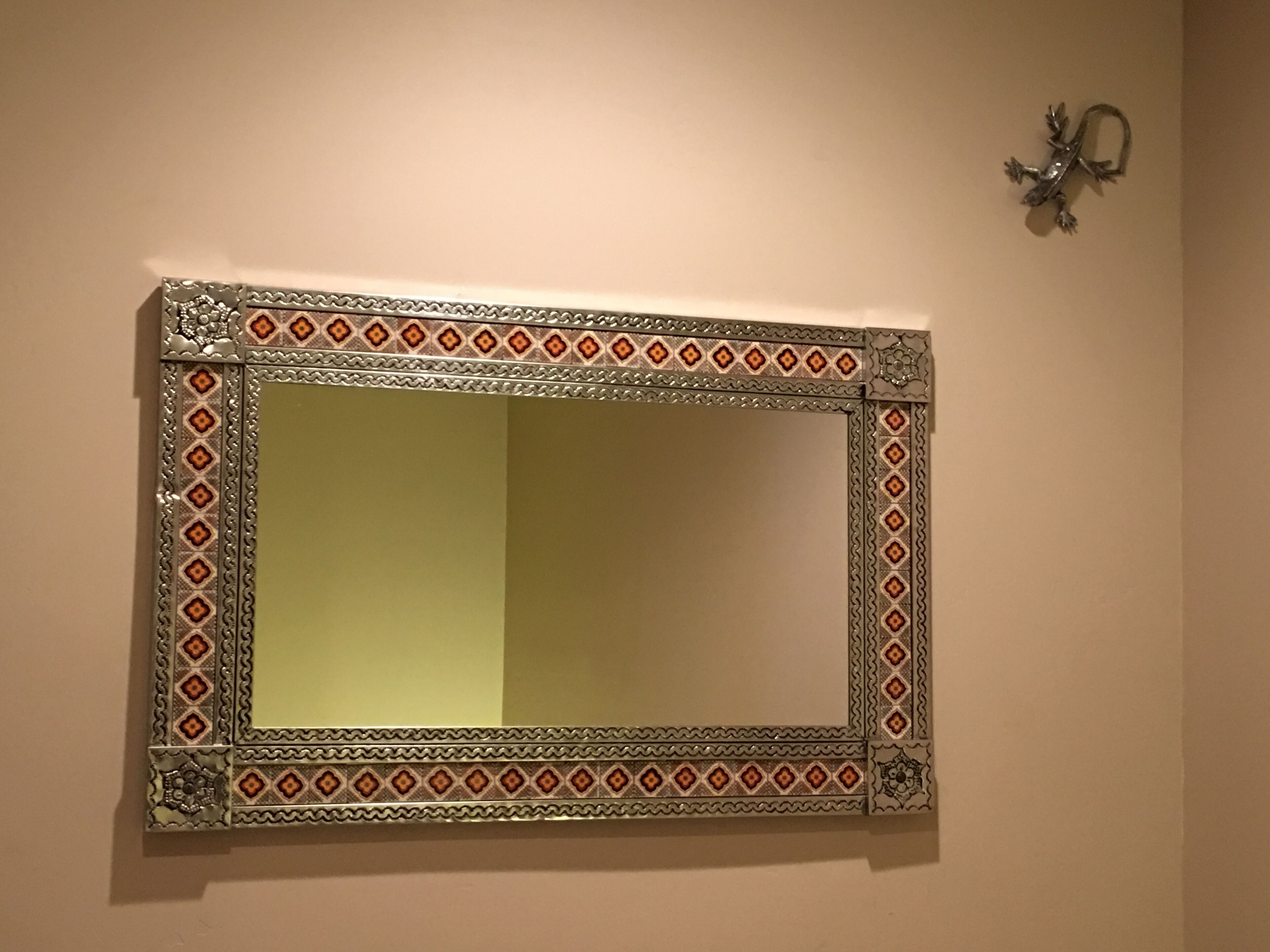 Un miroir rectangulaire doté d’un cadre en métal orné et d’une applique murale décorative sur le côté droit.
