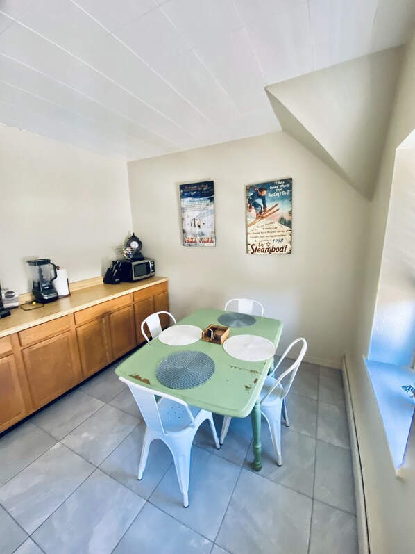 A small dining area with a green table, white chairs, and a wooden counter with a coffee maker. - Oldtown Fort Collins, Colorado (Fort Collins)