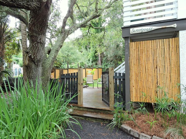 A wooden deck leading to a building with a bamboo fence and a sign that reads "Sweetgrass."