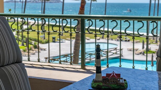 A balcony with a view of a pool, palm trees, and the ocean.