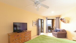 A bedroom with a bed, a television on a wooden dresser, a ceiling fan, and a view through an open door.