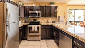 A modern kitchen with dark cabinets, stainless steel appliances, granite countertops, and a view of the ocean through the sliding glass door.