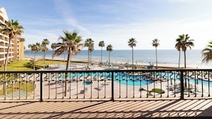 A pool area with lounge chairs and palm trees, overlooking a beach and ocean.