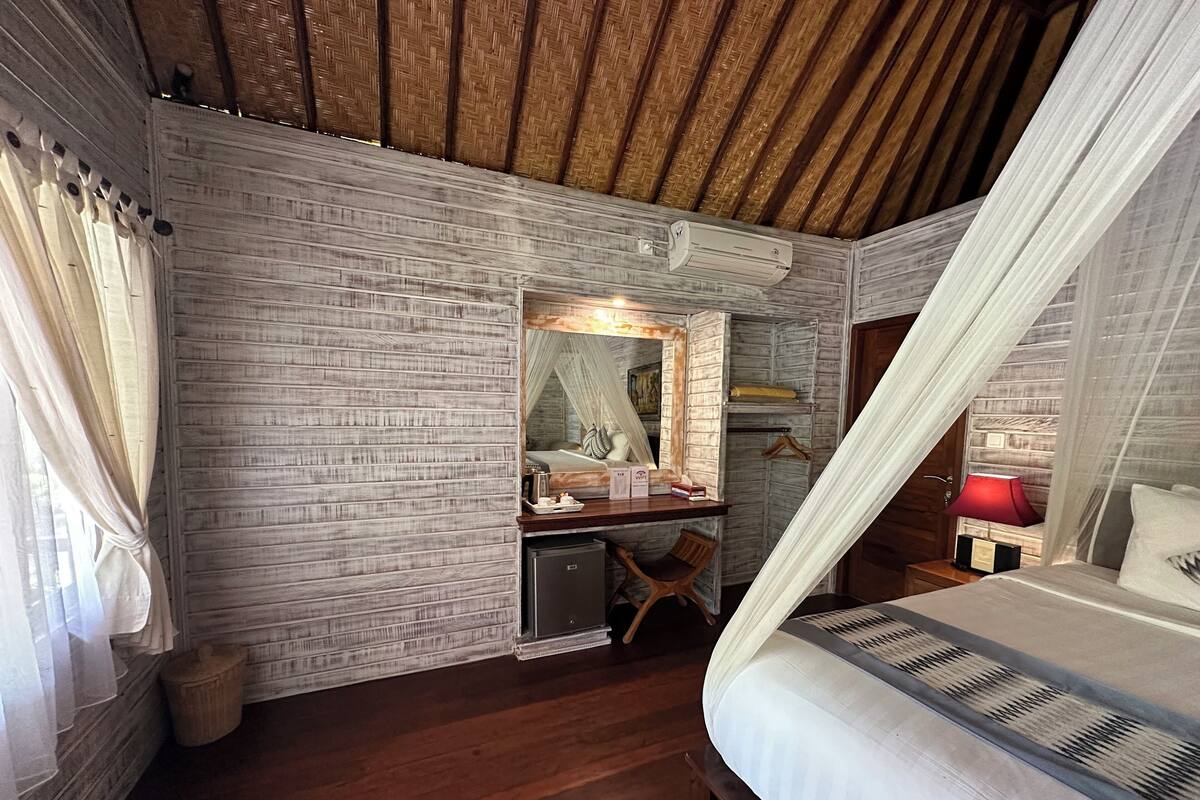 Un dormitorio con techo de madera, una cama con dosel, una mesita de noche con lámpara, un escritorio con espejo y un mueble pequeño.