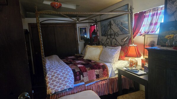 Una cama con dosel con un edredón estampado, una mesita de noche con lámpara y un espejo en la pared.