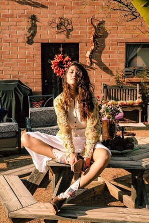 A person sitting on a wooden bench outdoors with a brick building in the background. - Knightly's Ranch Guesthouse  (Tucson)