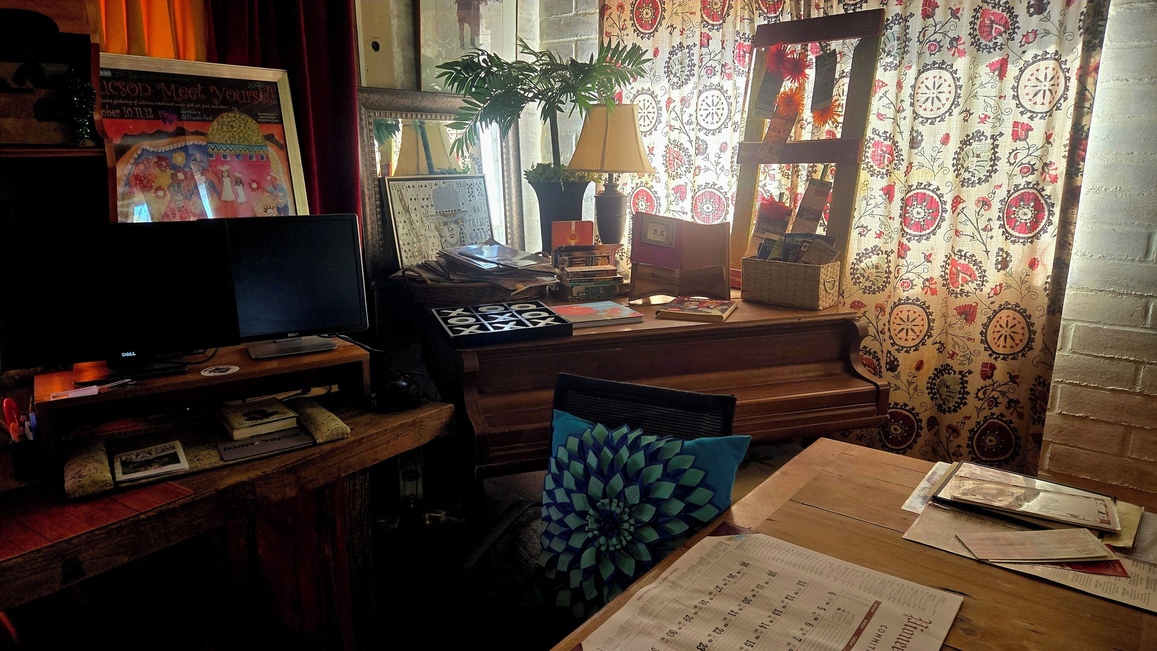 A room with a desk, a computer, a lamp, a plant, and a patterned curtain.